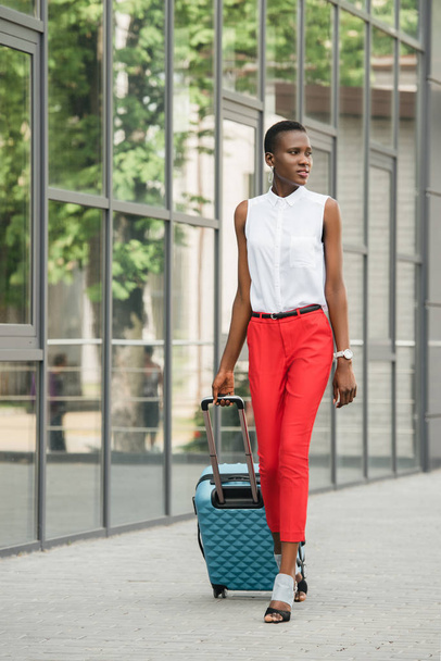 elegante atractiva mujer de negocios afroamericana caminando con bolsa de viaje en la calle y mirando hacia otro lado
 - Foto, Imagen