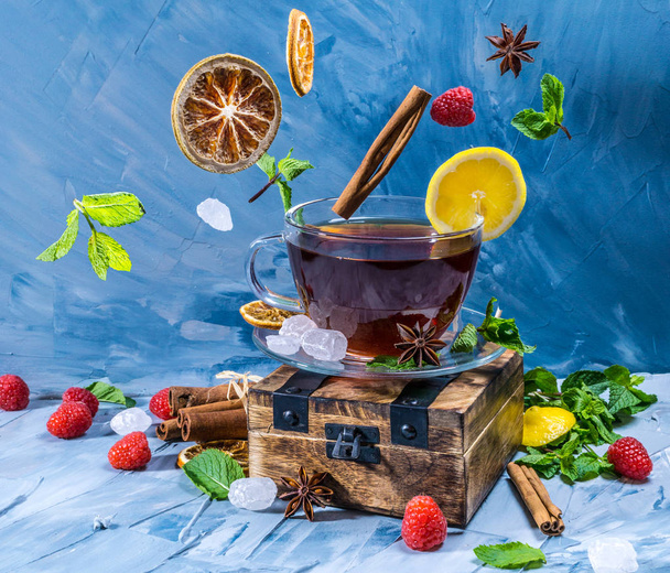 Magical tea concept. Levitating effect. Flying in air ingredients for tea, such as lemon, raspberry, mint leaves and sugar on blue background - Valokuva, kuva