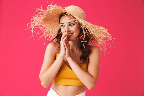 Image of stylish european woman 20s wearing big straw hat smiling and looking aside isolated over pink background - Foto, Bild