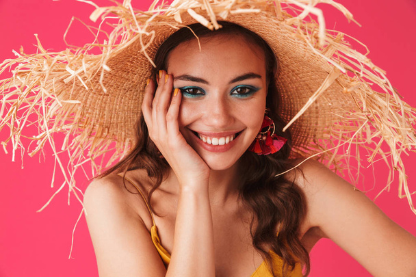 Portrait closeup of stylish content woman 20s wearing big straw hat smiling and holding cheek isolated over pink background - Фото, зображення