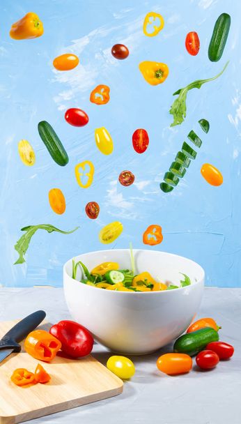 Levitating mixed vegetables on blue background. Magical cucumber, tomato and paprika with white bowl - Фото, зображення