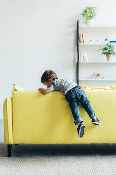 Kleiner Junge klettert zu Hause auf gelbem Sofa hoch - Foto, Bild