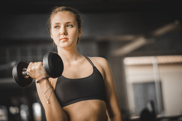 Fit beautiful young woman caucasian posing at the camera in sportswear. Young woman holding dumbbell during an exercise class in a gym. Healthy sports lifestyle, Fitness concept. With copy space. - Photo, Image