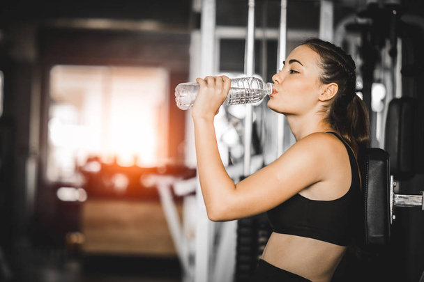 Fit young woman caucasian sitting and resting after workout or exercise in fitness gym. woman at gym taking a break and relax with water in sportswear. Fitness concept, Healthy, Sport, Lifestyle - Zdjęcie, obraz