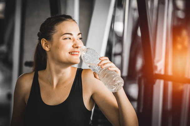 Fit young woman caucasian sitting and resting after workout or exercise in fitness gym. woman at gym taking a break and relax with water in sportswear. Fitness concept, Healthy, Sport, Lifestyle - 写真・画像