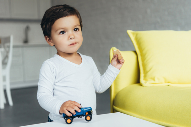 adorable boy playing with toy car and eating cookie - 写真・画像