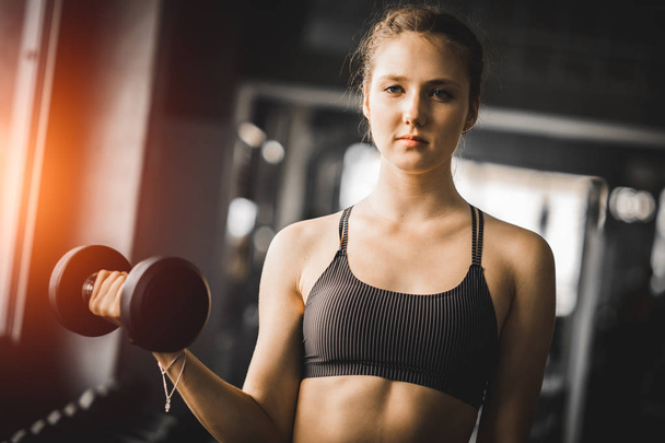 Fit beautiful young woman caucasian posing at the camera in sportswear. Young woman holding dumbbell during an exercise class in a gym. Healthy, sports, lifestyle, Fitness concept. With copy space. - Foto, imagen