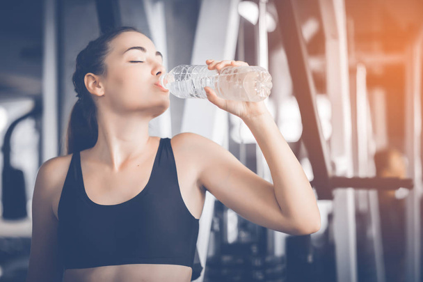 Fit young woman caucasian sitting and resting after workout or exercise in fitness gym. woman at gym taking a break and relax with water in sportswear. Fitness concept, Healthy, Sport, Lifestyle - Foto, Bild