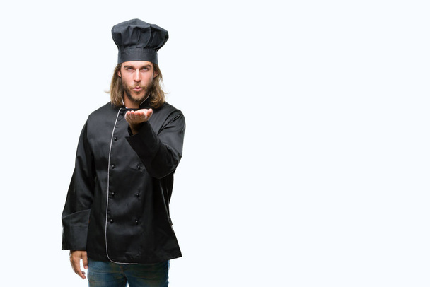Young handsome cook man with long hair over isolated background looking at the camera blowing a kiss with hand on air being lovely and sexy. Love expression. - Photo, Image