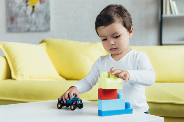 little boy playing with constructor blocks and toy car on table at home - Foto, Imagem