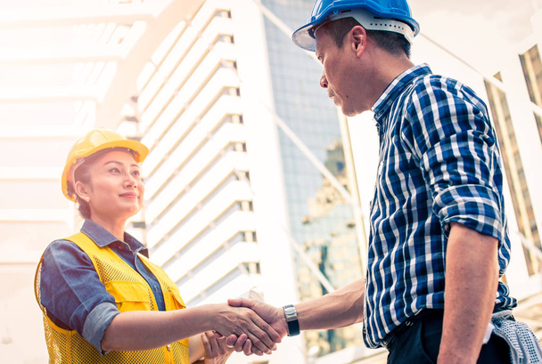 Construction and engineer concept. Construction worker in protective uniform shaking hands meeting for architectural project working with partner. Worker and customer having agreement in factory. - Foto, Imagen