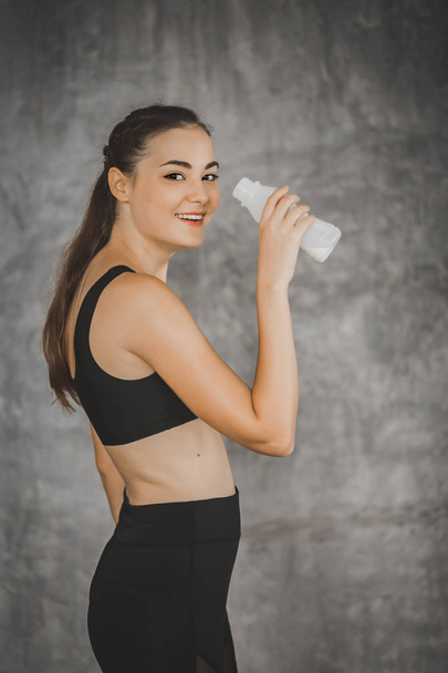 Fit young woman drinking milk from the bottle after exercise in gym. Beautiful woman at gym taking a break with health drink and smile in sportswear. Concept of healthy, fitness, sport, lifestyle. - Photo, Image