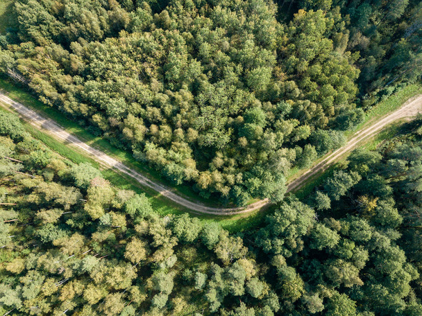 Drohnenbild. Luftaufnahme der ländlichen Schotterstraße im grünen Wald und Bäume mit Schatten von oben an sonnigen Sommertagen. Lettland - Foto, Bild
