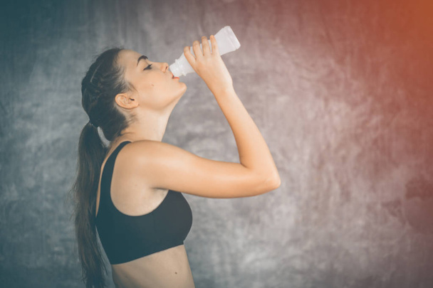 Fit young woman drinking milk from the bottle after exercise in gym. Beautiful woman at gym taking a break with health drink and smile in sportswear. Concept of healthy, fitness, sport, lifestyle. - Fotó, kép