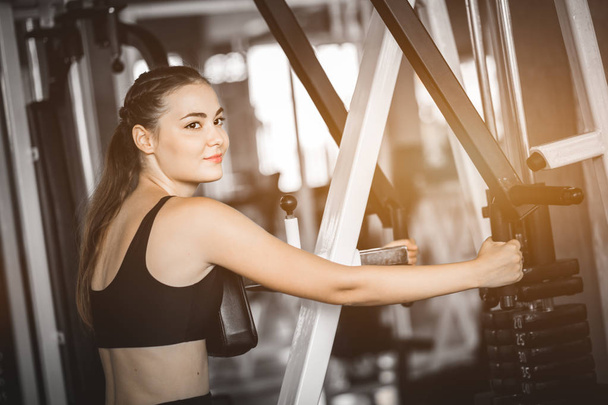 Fit beautiful young woman exercise workout on machine in gym. Glad smiling girl is enjoy with her training process. Concept of fitness, Healthy, Sport, Lifestyle - Valokuva, kuva