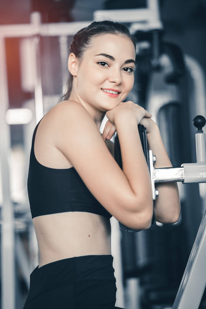 Fit beautiful young woman exercise workout on machine in gym. Glad smiling girl is enjoy with her training process. Concept of fitness, Healthy, Sport, Lifestyle - Zdjęcie, obraz