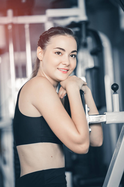 Fit beautiful young woman exercise workout on machine in gym. Glad smiling girl is enjoy with her training process. Concept of fitness, Healthy, Sport, Lifestyle - Photo, Image