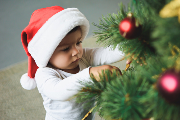 adorable kid in santa hat decorating christmas tree - Valokuva, kuva