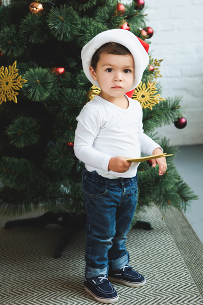 cute boy in santa hat holding star while decorating christmas tree - Photo, Image