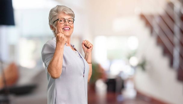 Hermosa mujer mayor muy feliz y emocionada, levantando brazos, celebrando una victoria o éxito, ganando la lotería en casa
. - Foto, Imagen