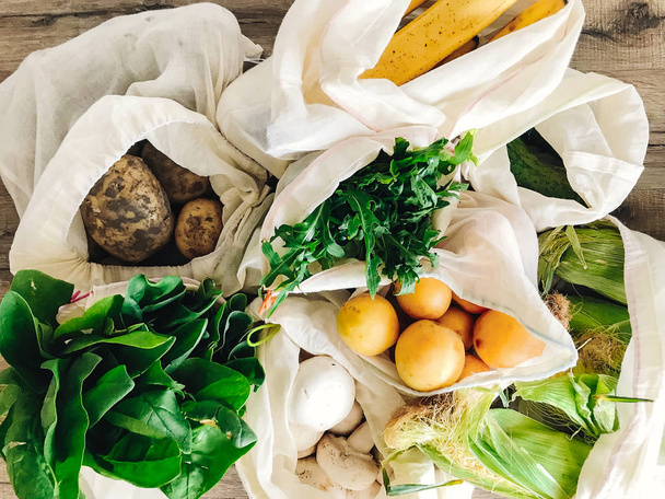 Zero Waste Shopping Konzept. frisches Gemüse in Öko-Baumwolltaschen auf dem Tisch in der Küche. Salat, Mais, Kartoffeln, Aprikosen, Bananen, Rucola, Pilze vom Markt. Verbot von Plastik - Foto, Bild