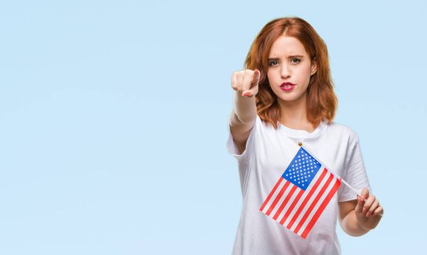 Jovem bela mulher segurando bandeira da América sobre fundo isolado apontando com o dedo para a câmera e para você, sinal de mão, gesto positivo e confiante da frente
 - Foto, Imagem