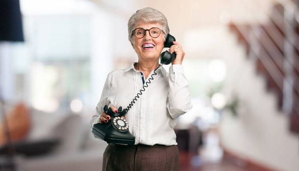 Belle femme âgée riant à haute voix, s'amusant avec la conversation, appelant un ami ou un client à la maison
. - Photo, image