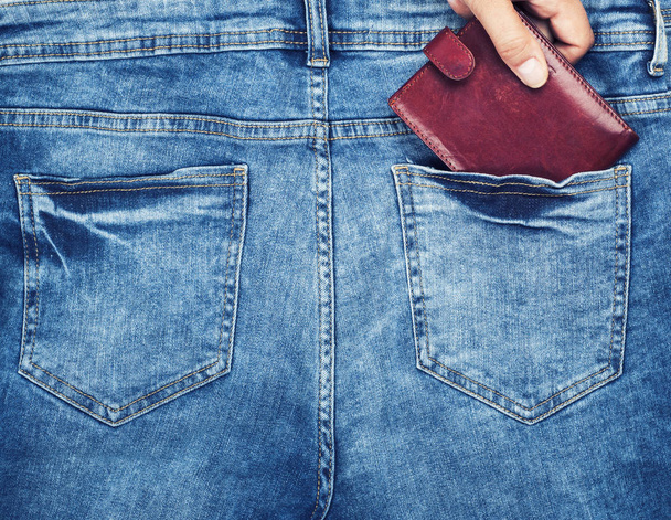 braune Ledertasche liegt in der Gesäßtasche einer blauen Jeans, eine weibliche Hand klammert sich an eine Handtasche - Foto, Bild