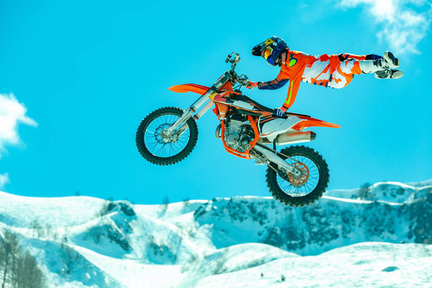 racer on a motorcycle in flight, jumps and takes off on a springboard against the snowy mountains - Photo, Image