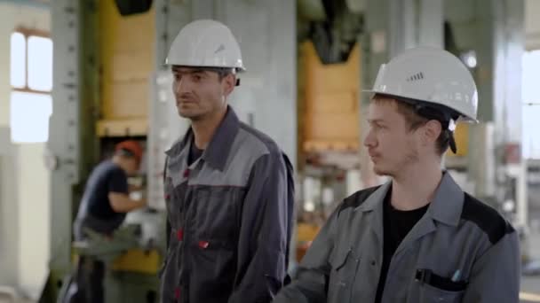 Zwei Arbeiter stehen in der Produktionshalle mit großen Drehmaschinen. - Filmmaterial, Video