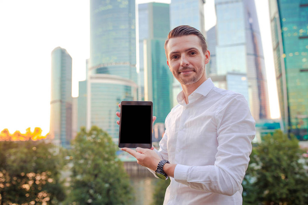 Homme d'affaires utilisant un ordinateur portable à l'extérieur dans la ville urbaine avec des gratte-ciel bâtiments en arrière-plan. Affichage noir rapproché de l'ordinateur portable pour votre publicité
 - Photo, image