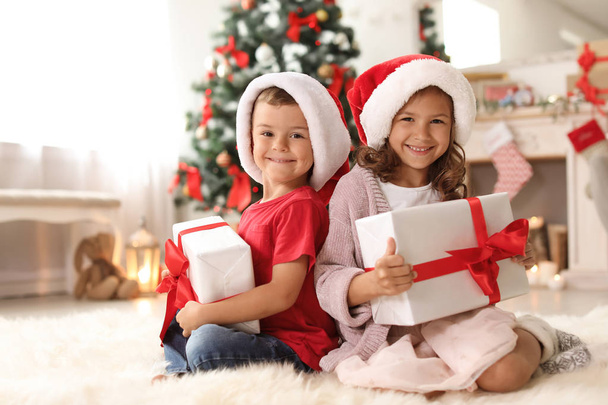 Cute little children in Santa hats with Christmas gift boxes at home - Foto, Imagem