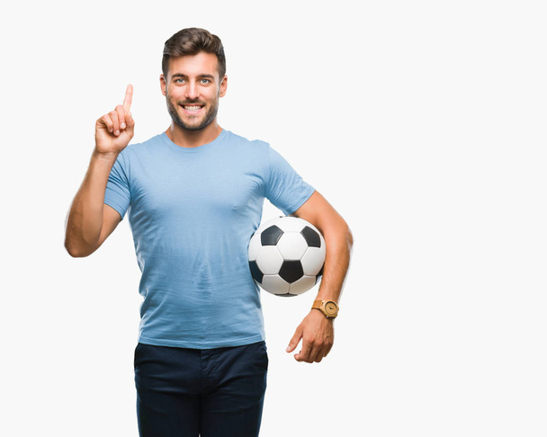 Nuori komea mies, jolla on jalkapallo jalkapallo eristetty tausta yllättynyt ideasta tai kysymyksestä, joka osoittaa sormella onnellisia kasvoja, numero yksi
 - Valokuva, kuva