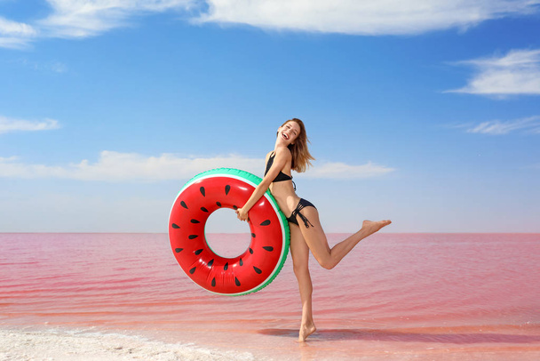 Beautiful woman with inflatable ring posing near pink lake on sunny day - Фото, зображення