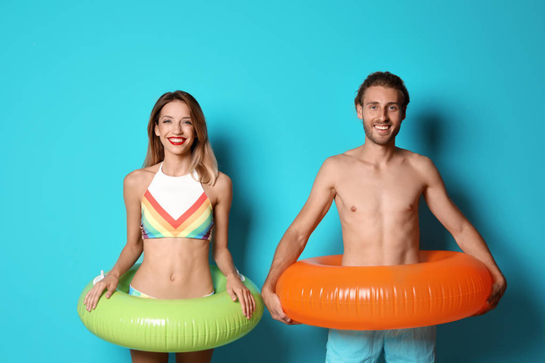 Happy young couple in beachwear with inflatable rings on color background - Фото, зображення