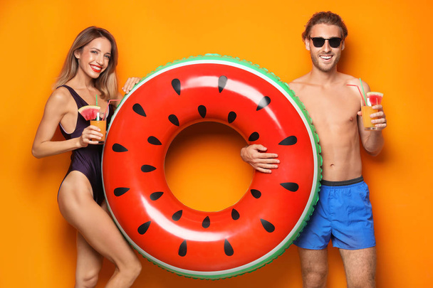 Happy young couple in beachwear with inflatable ring and cocktails on color background - Фото, зображення