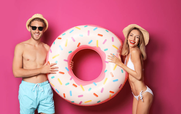 Happy young couple in beachwear with inflatable ring on color background - Foto, Bild