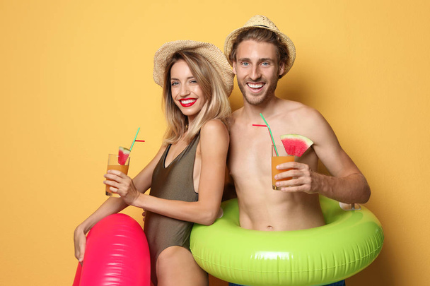 Feliz pareja joven en ropa de playa con anillos inflables y cócteles en el fondo de color
 - Foto, Imagen