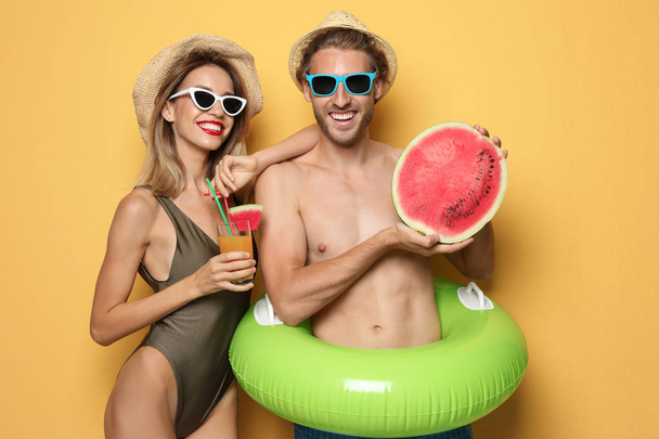 Happy young couple in beachwear with inflatable ring and cocktail on color background - Valokuva, kuva