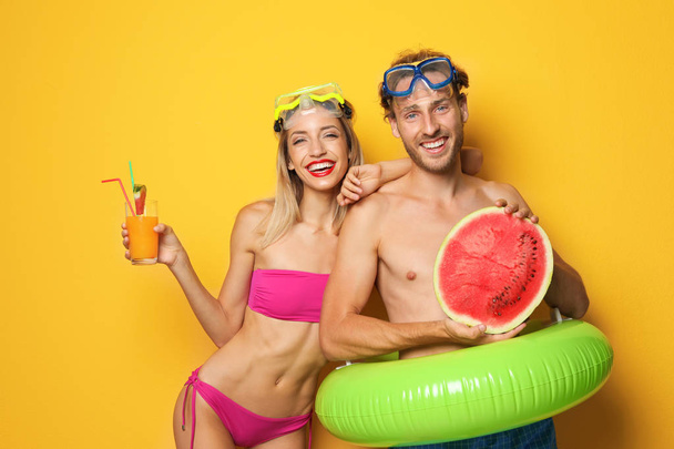 Happy young couple in beachwear with inflatable ring and cocktail on color background - Фото, зображення