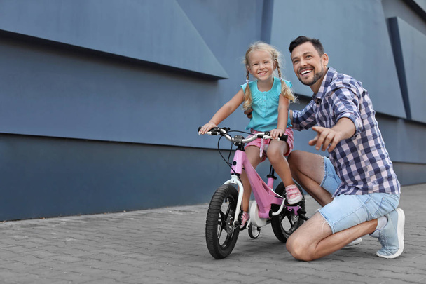 Father teaching daughter to ride bicycle on street - Foto, afbeelding