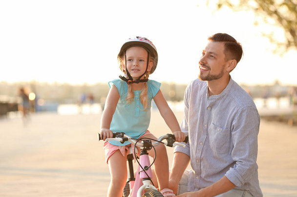 Father teaching daughter to ride bicycle on street - Foto, immagini