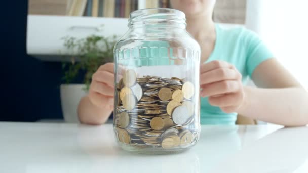4k video of young woman sticking title Savings on glass jar full of coins - Footage, Video