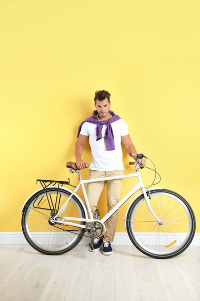 Handsome young hipster man with bicycle near yellow wall - Foto, immagini