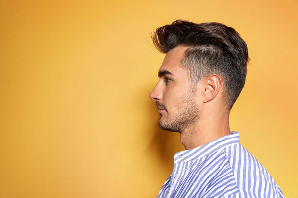 Young man with trendy hairstyle posing on color background - Foto, afbeelding