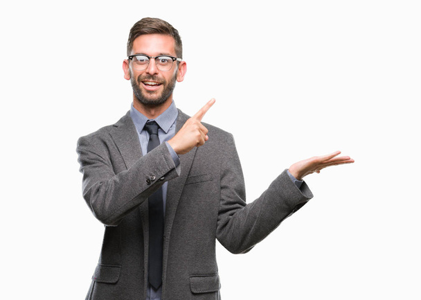 Young handsome business man over isolated background amazed and smiling to the camera while presenting with hand and pointing with finger. - Photo, Image