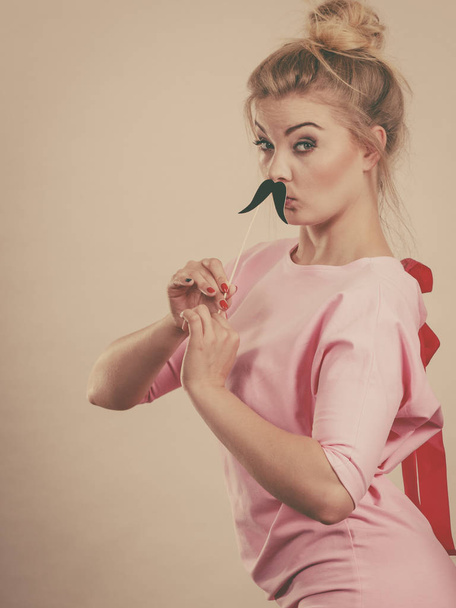 Happy woman holding fake moustache on stick having fun. Photo and carnival funny accessories concept. - 写真・画像
