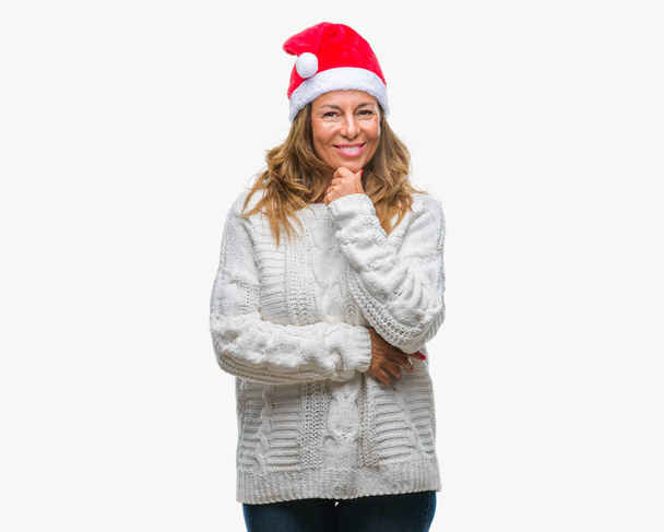 Старша іспаномовна жінка в різдвяному капелюсі над ізольованим тлом впевнено дивиться на камеру з посмішкою з схрещеними руками і піднятою рукою на підборідді. Мислення позитивне
. - Фото, зображення