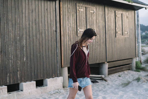 Chica joven con teléfono inteligente al aire libre junto a la casa de madera
 - Foto, Imagen