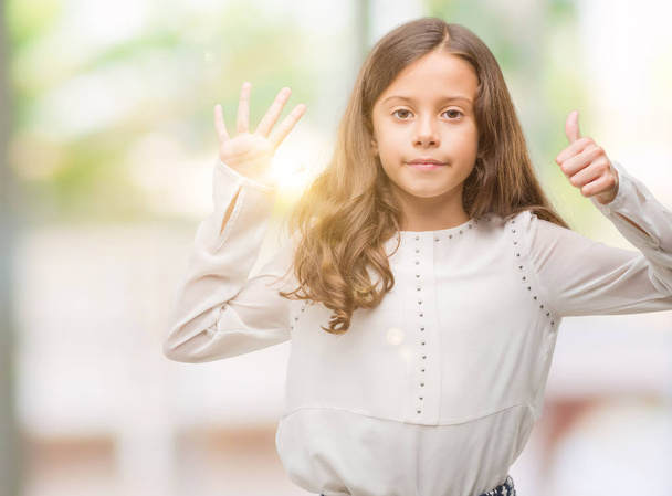 brünettes hispanisches Mädchen, das mit Fingern Nummer sechs nach oben zeigt und dabei selbstbewusst und glücklich lächelt. - Foto, Bild